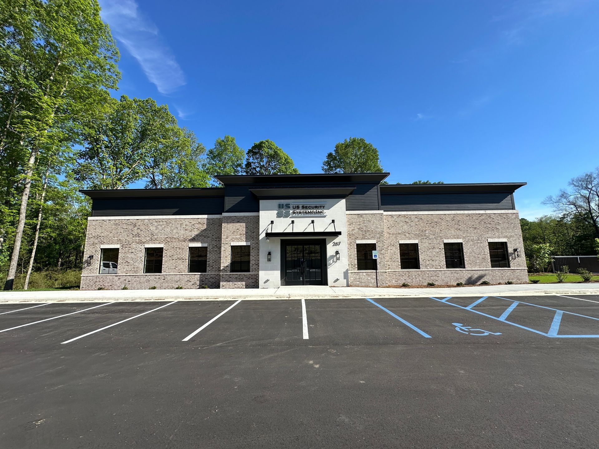 A modern, single-story brick office building with a central entrance under a sunny blue sky, fronted by a parking lot.