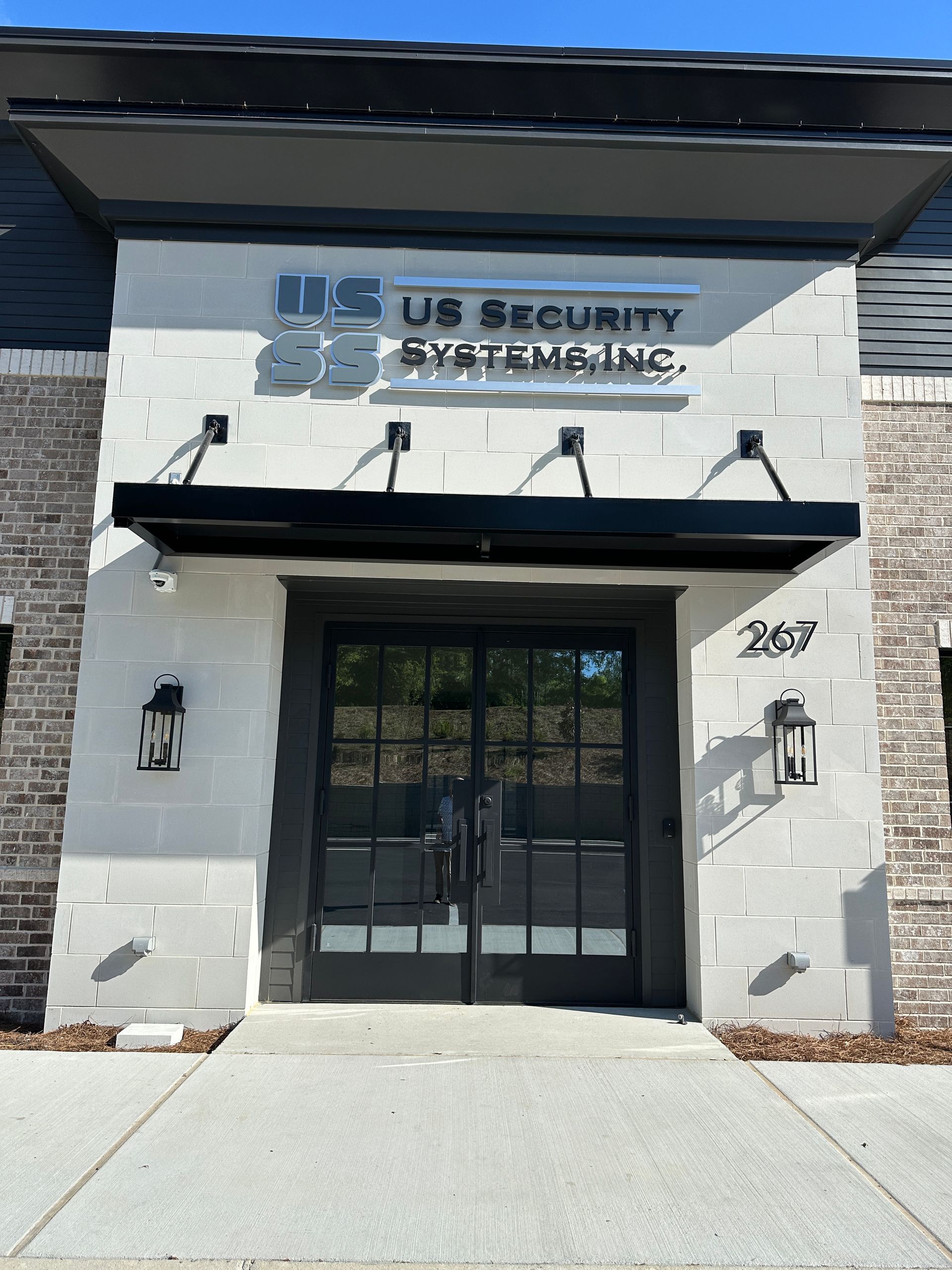 The building entrance for US Security Systems, Inc. with a black awning and glass double doors at suite number 207.