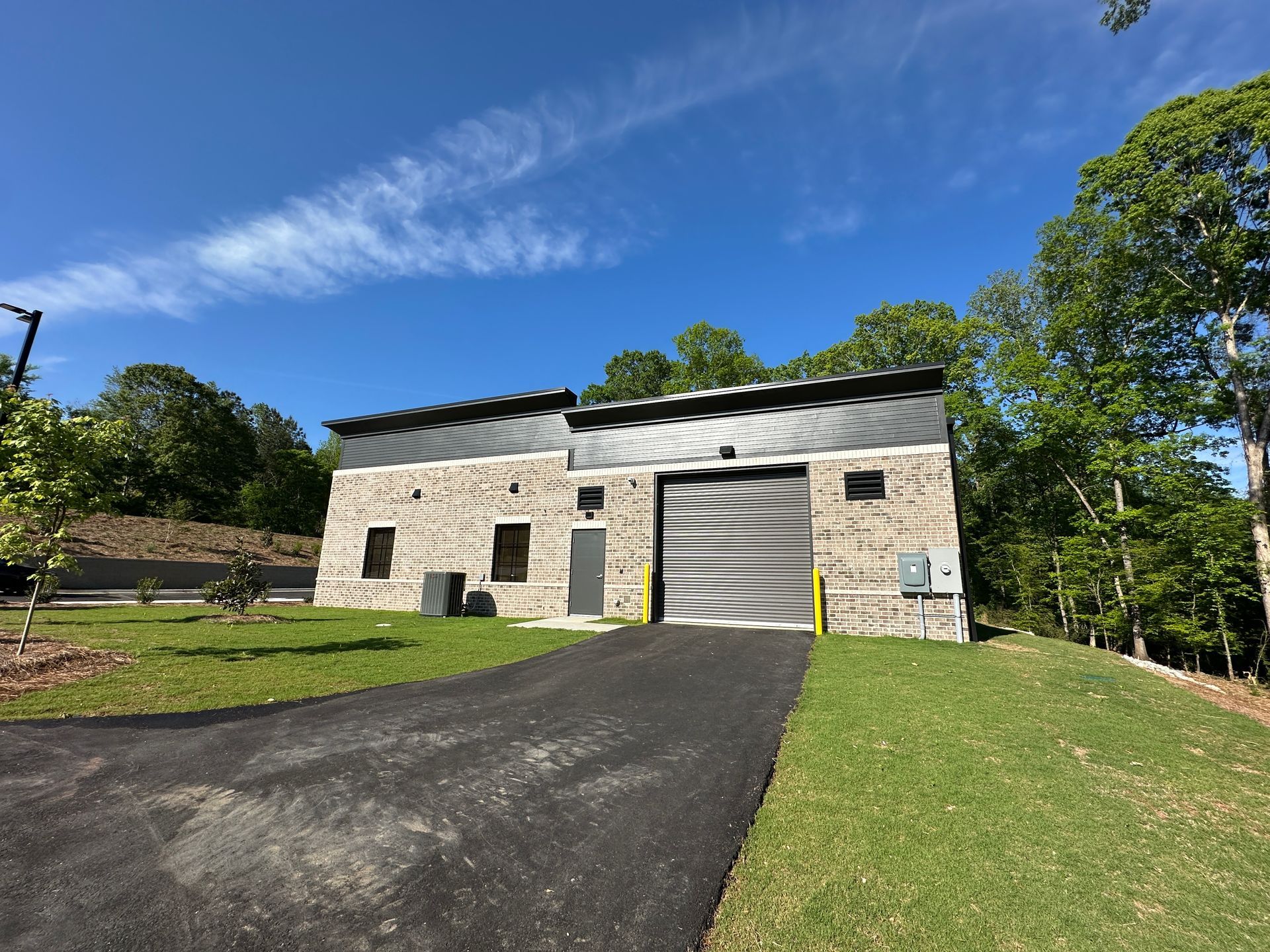 A single-story, stone-faced commercial building with a roll-up garage door and a metal roof under a bright blue sky.