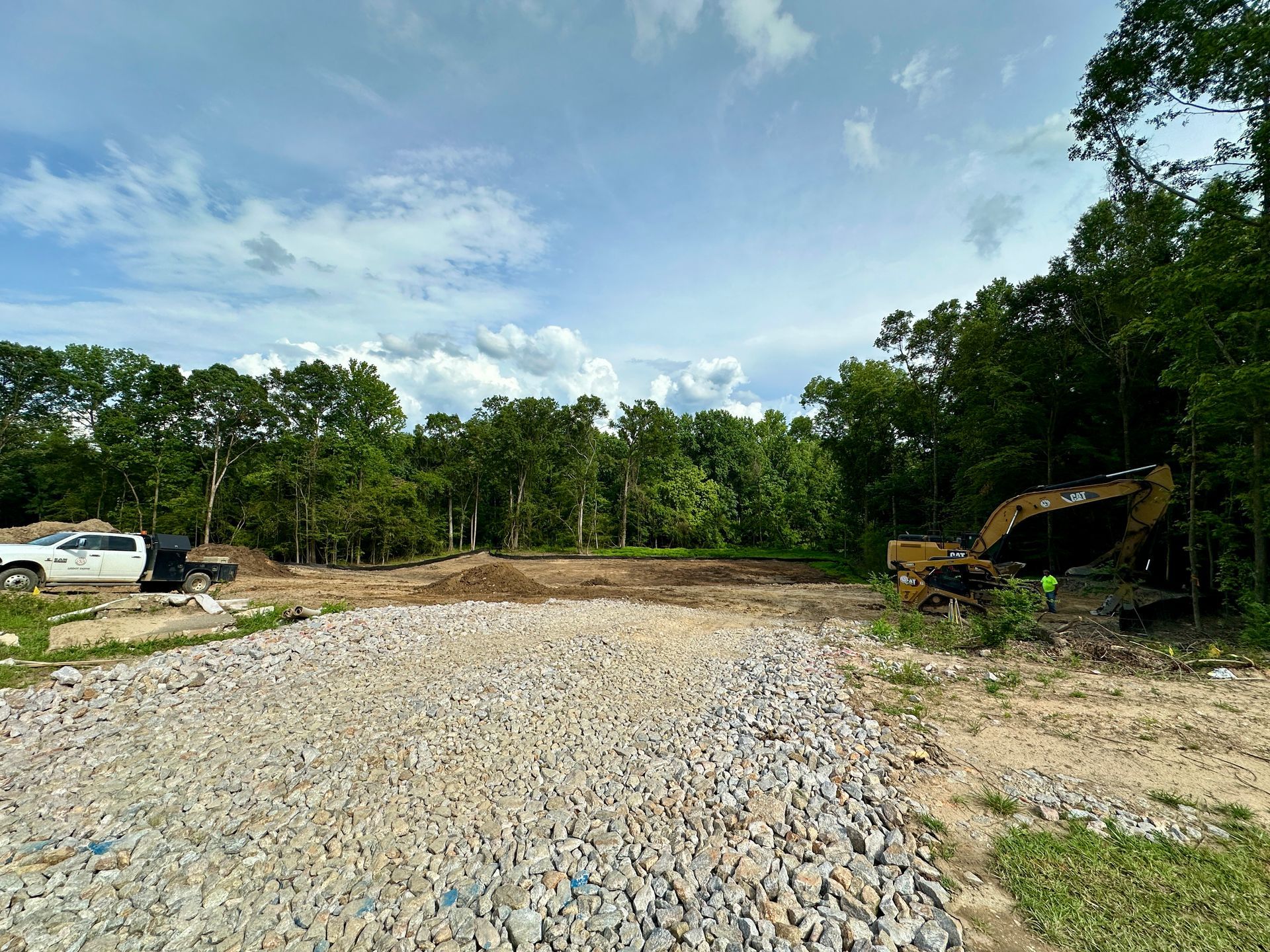 A construction site with a lot of gravel and trees in the background.