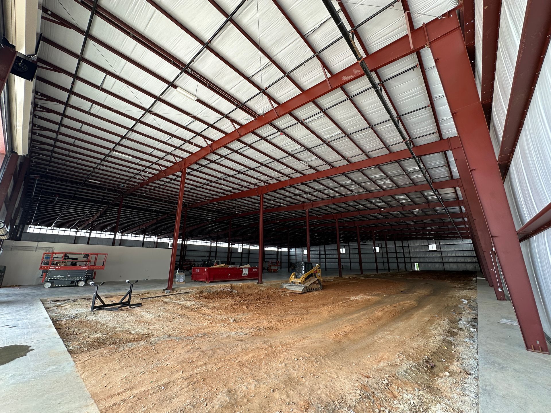Construction site: Interior of a large metal building with exposed red beams and dirt floor.