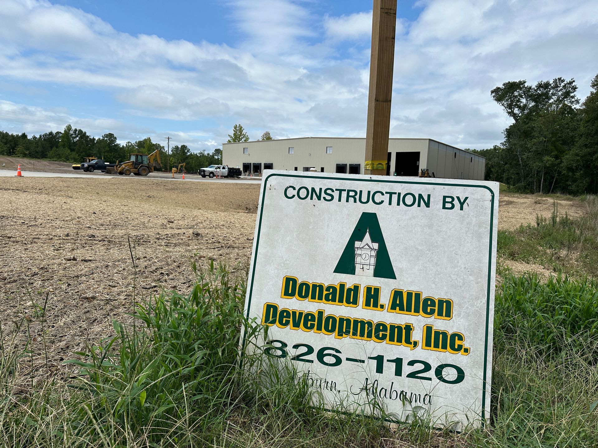 Construction site with sign for Donald H. Allen Development, Inc. In the background is a building and construction equipment.