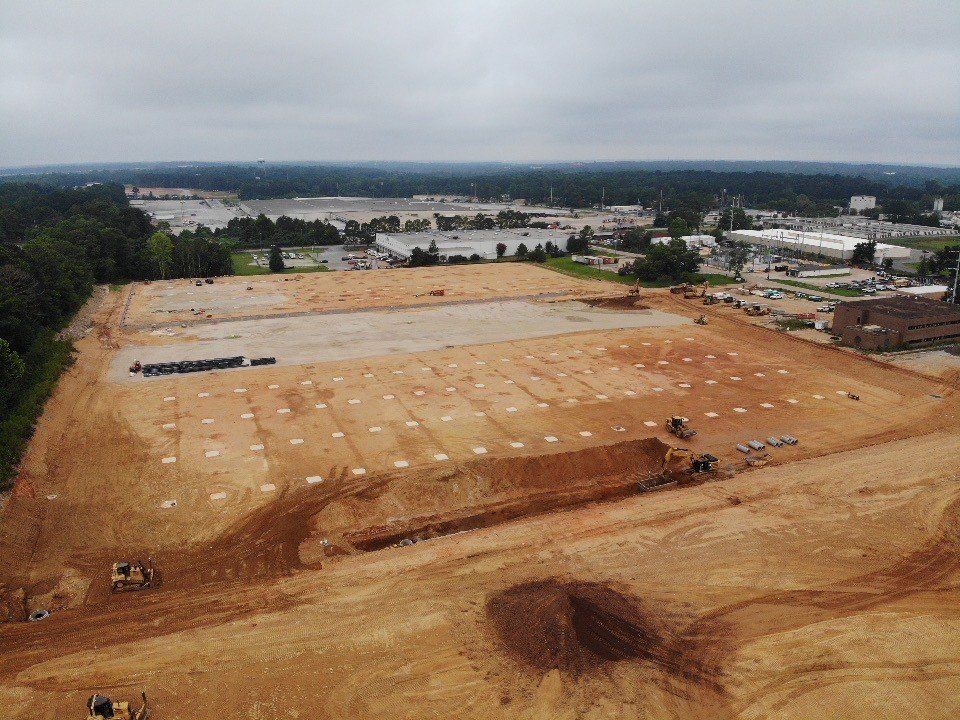 An aerial view of a large dirt field with buildings in the background.