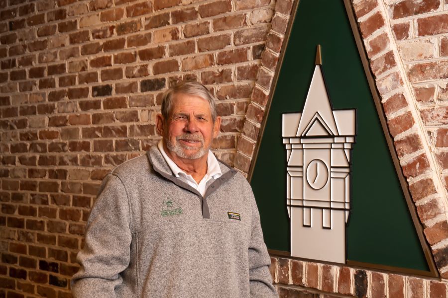 Rusty Lewis is standing in front of a brick wall with a clock tower on it.