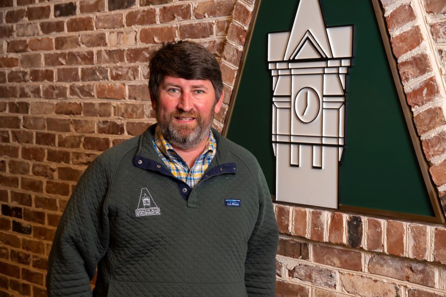 A man with a beard is standing in front of a brick wall.