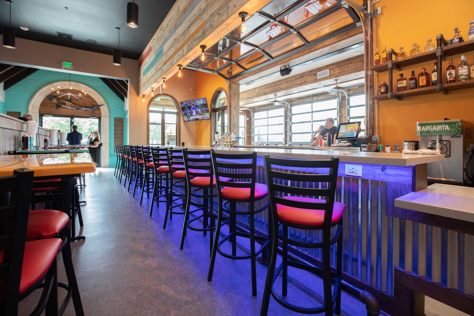 A restaurant with a long bar and tables and chairs.