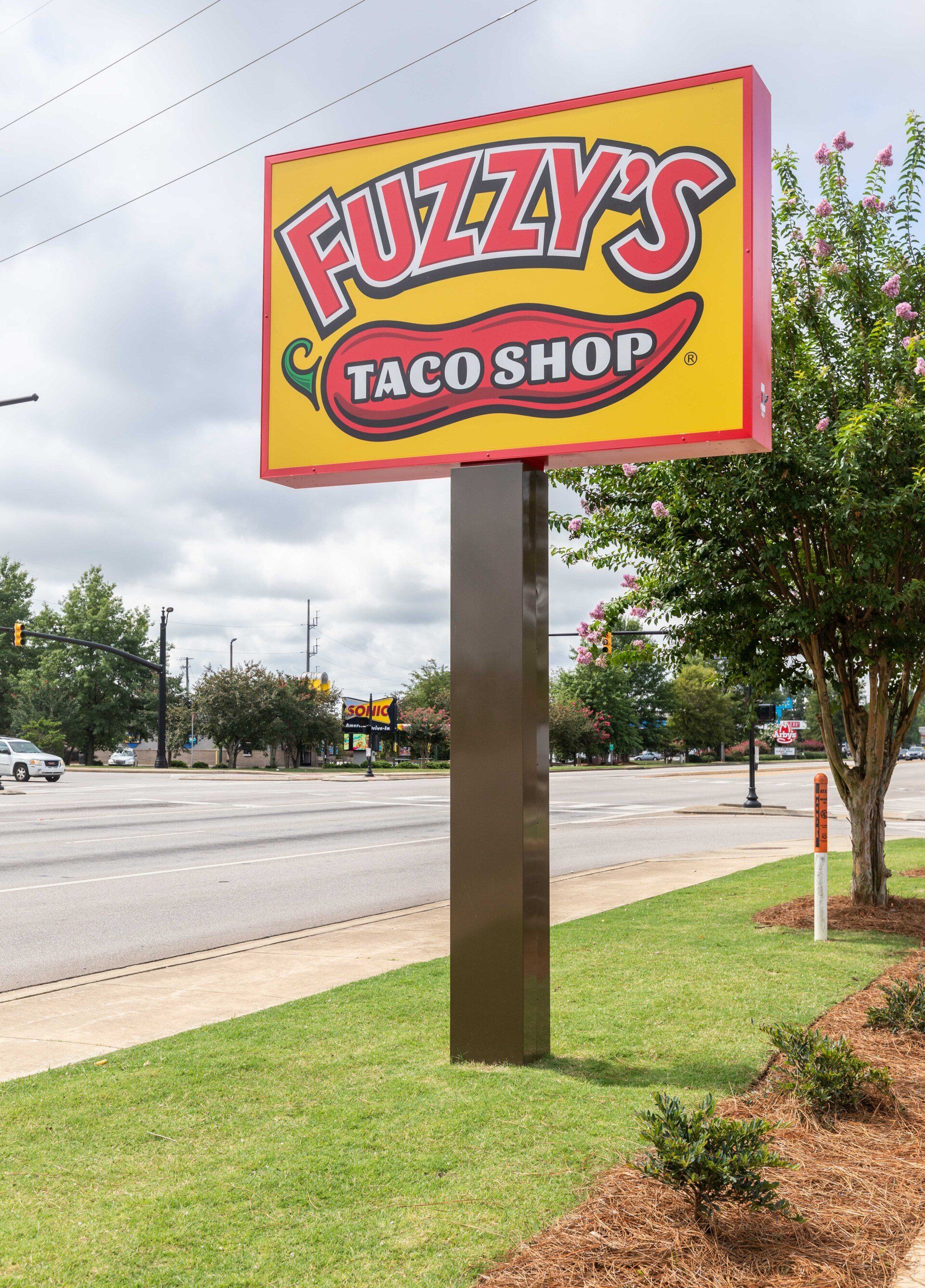 A fuzzy 's taco shop sign is on the side of the road