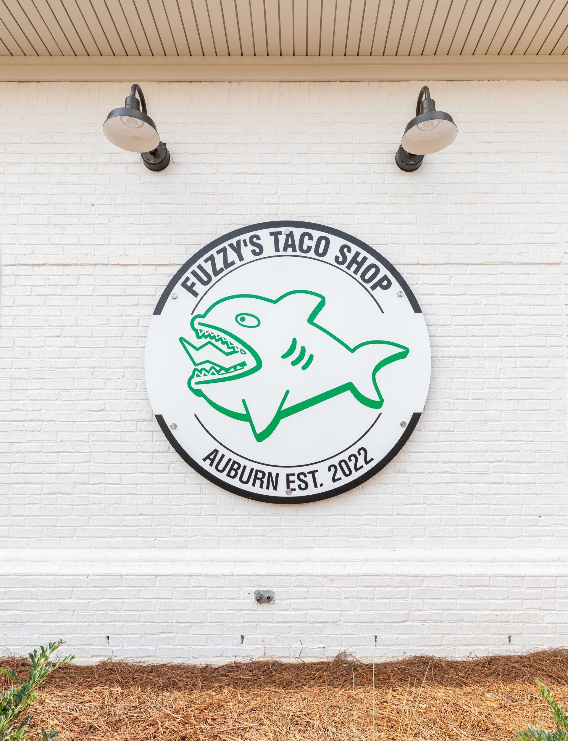 A fuzzy 's taco shop sign is on a white brick wall.