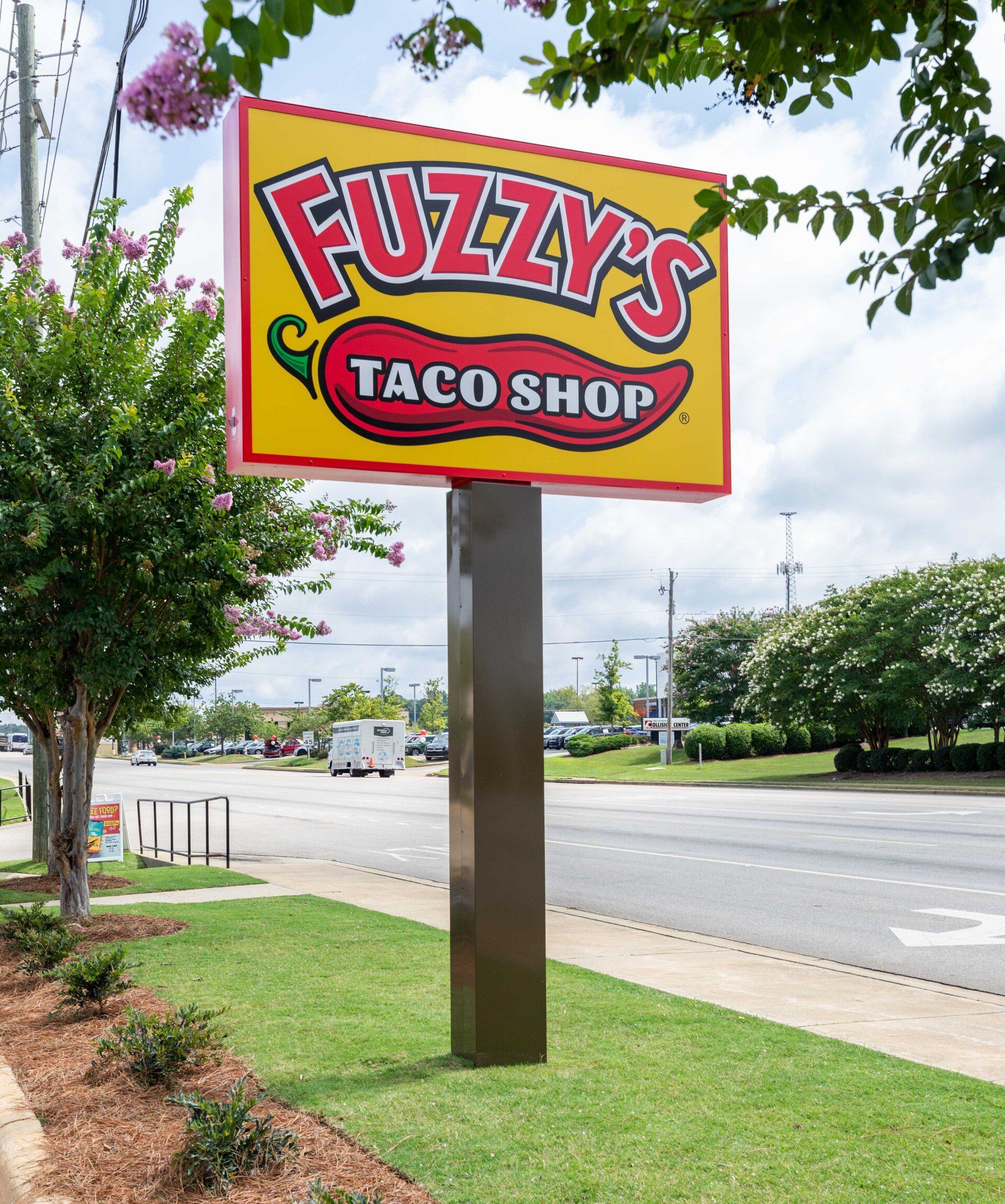 A fuzzy 's taco shop sign is sitting on the side of the road.