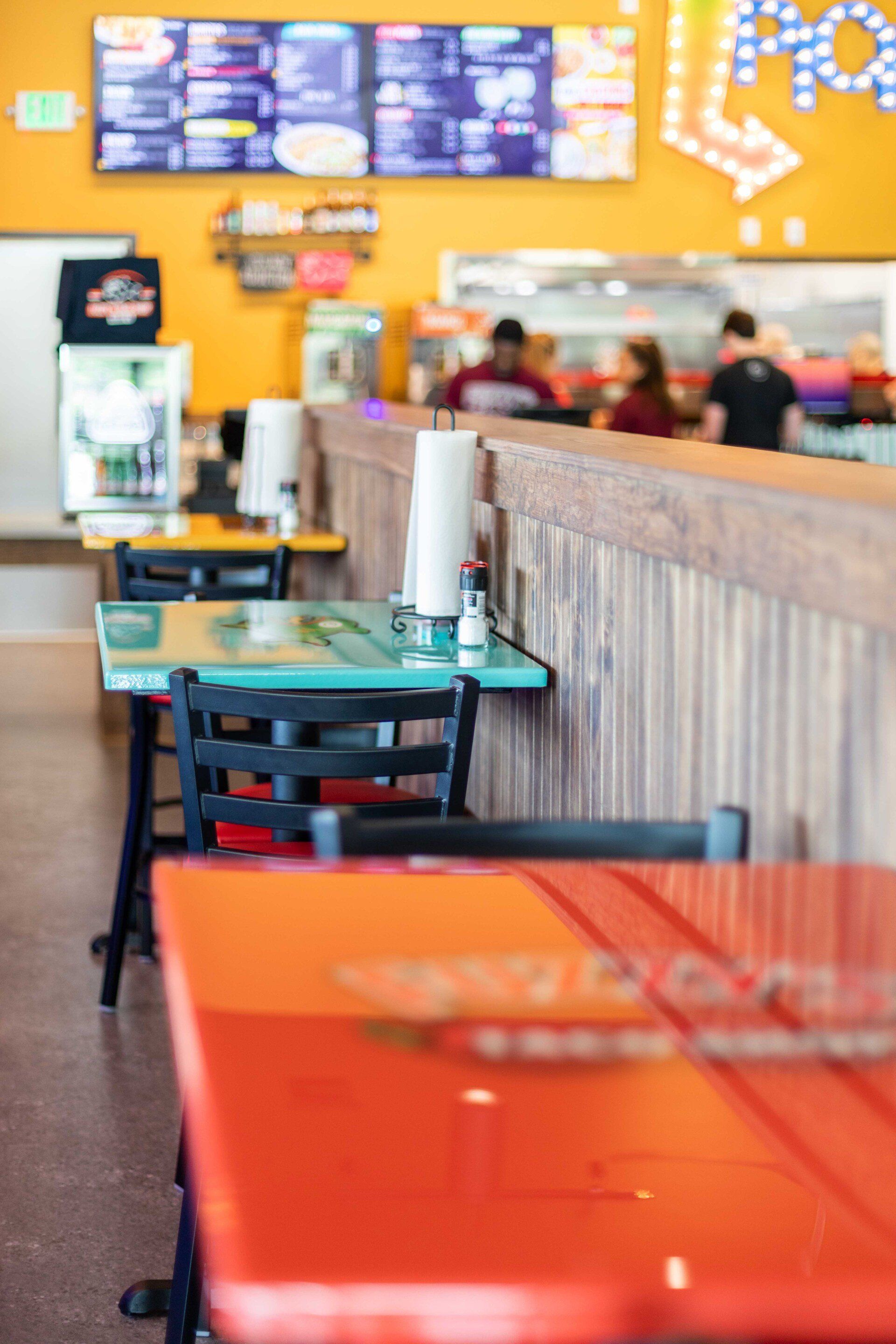 A restaurant with tables and chairs and a menu on the wall.