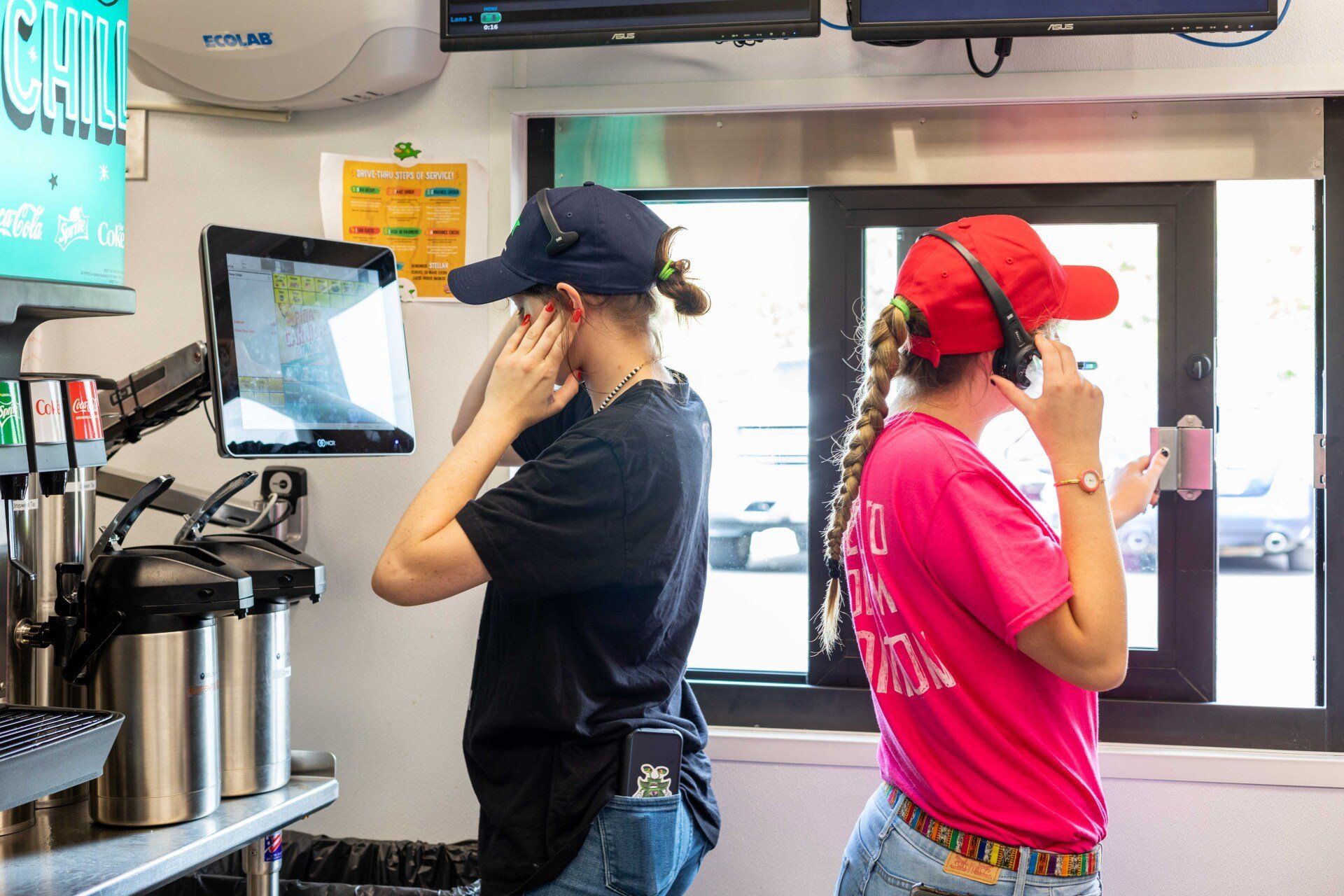 Two women are standing in a restaurant talking on their cell phones.