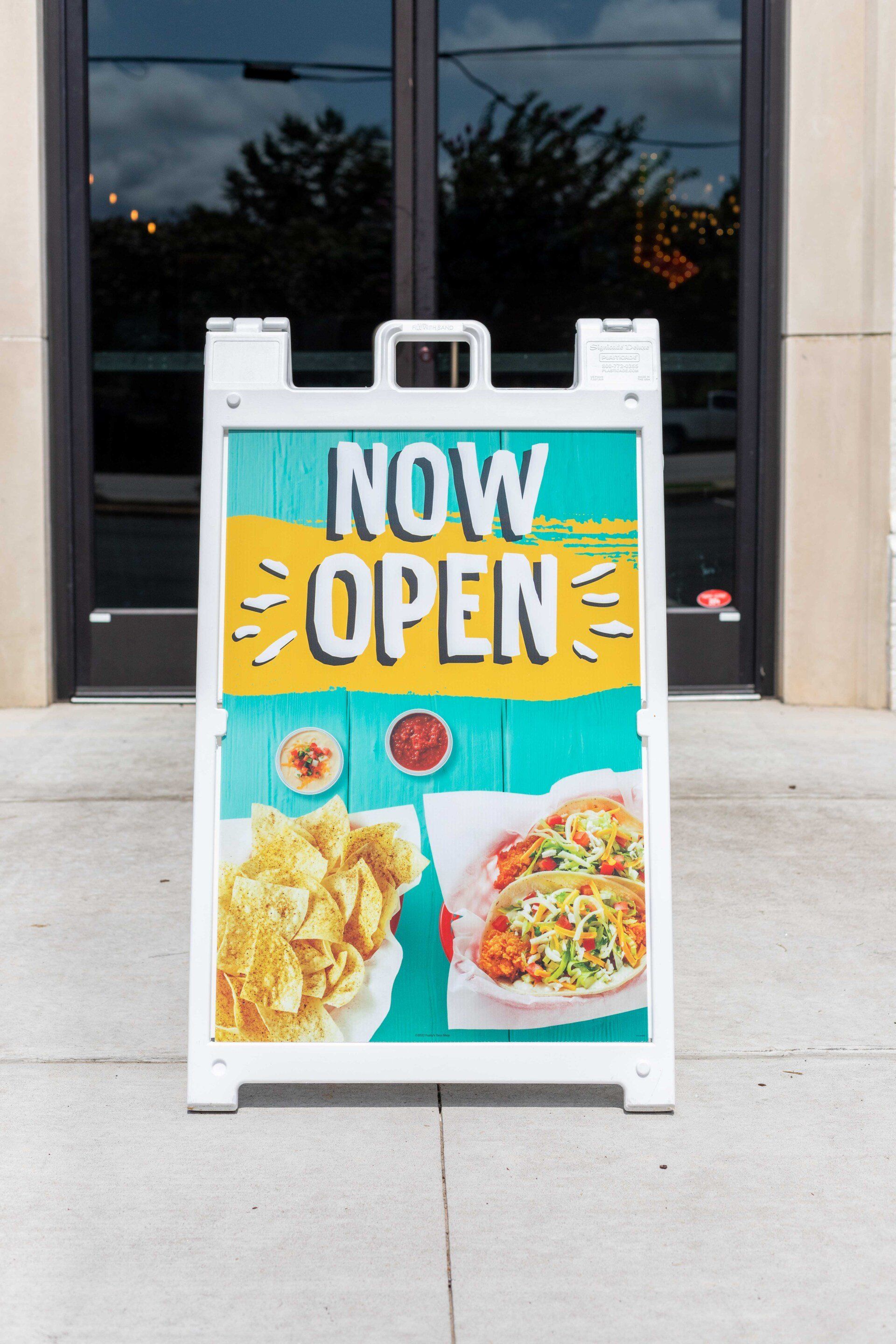A sign that says now open with a picture of food on it