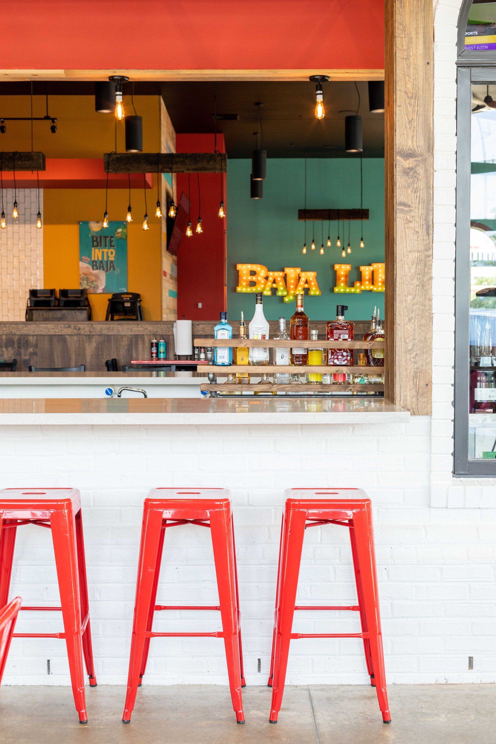 A restaurant with red stools and a bar.