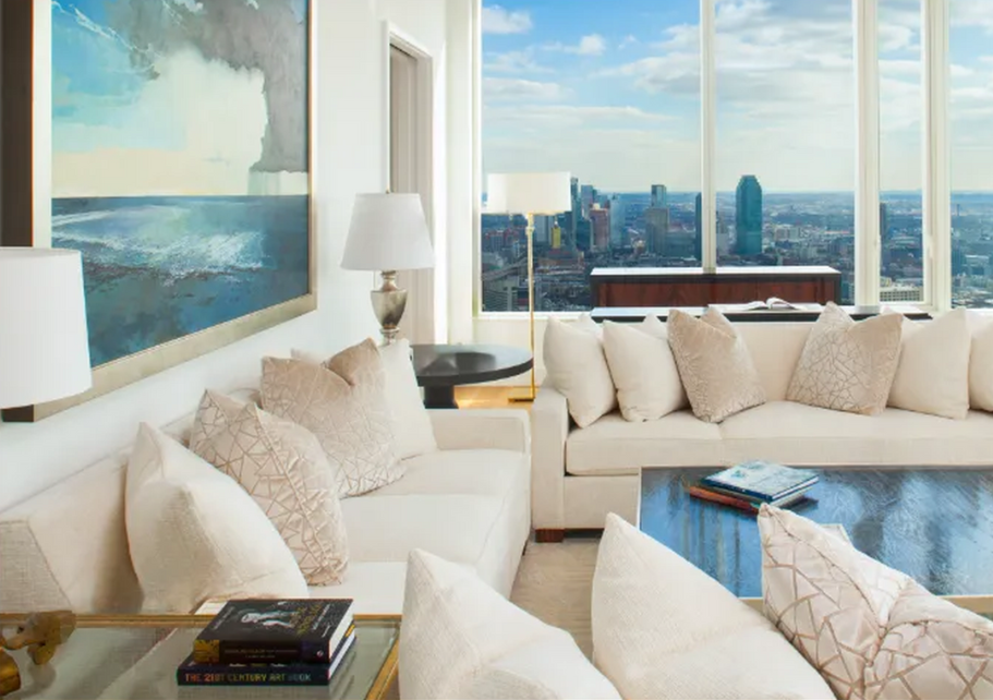 Elegant living room with white sofas, large windows overlooking a city skyline, and colorful abstract artwork.