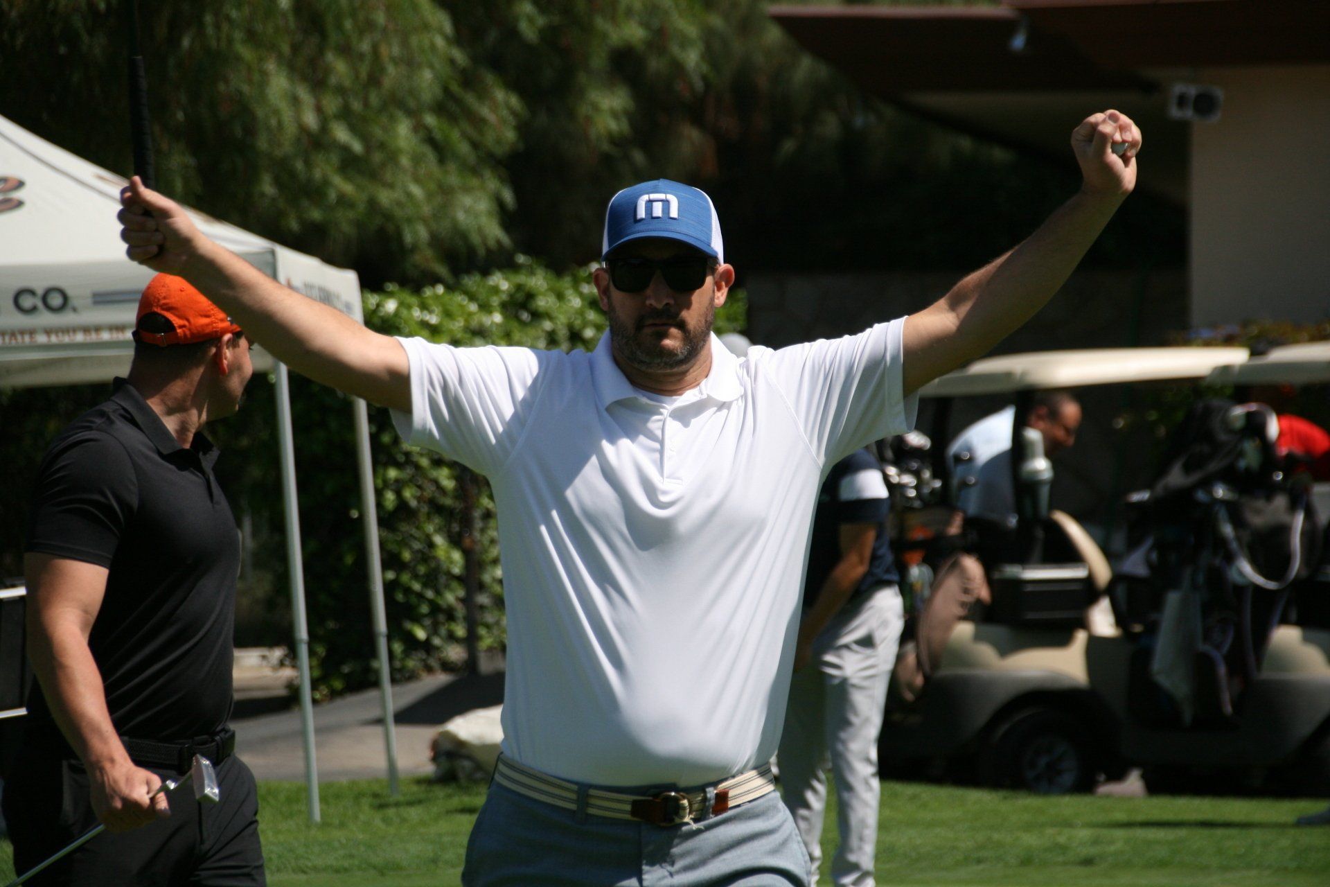 A man is standing on a golf course with his arms in the air.