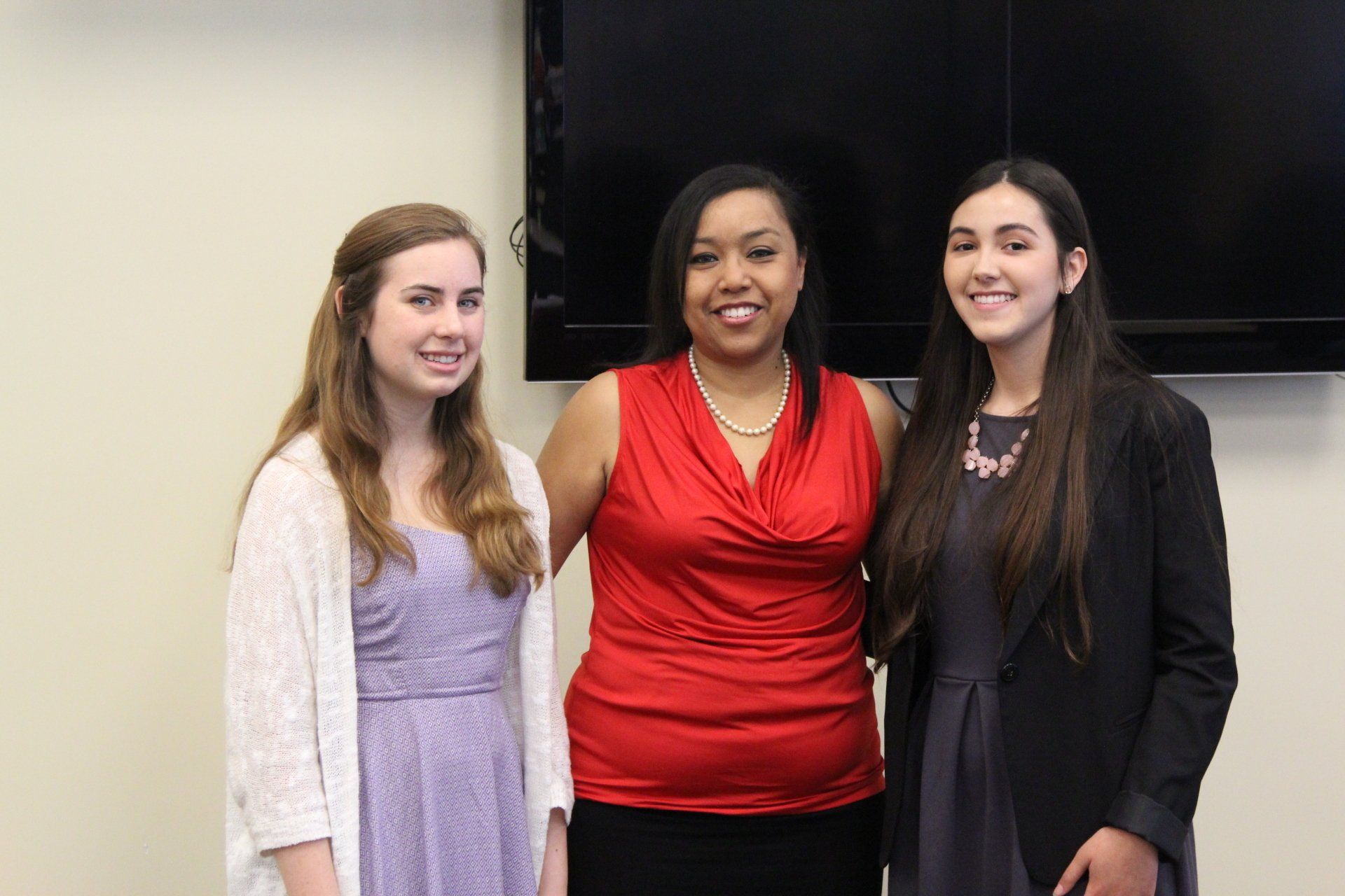 Three women are posing for a picture in front of a television.