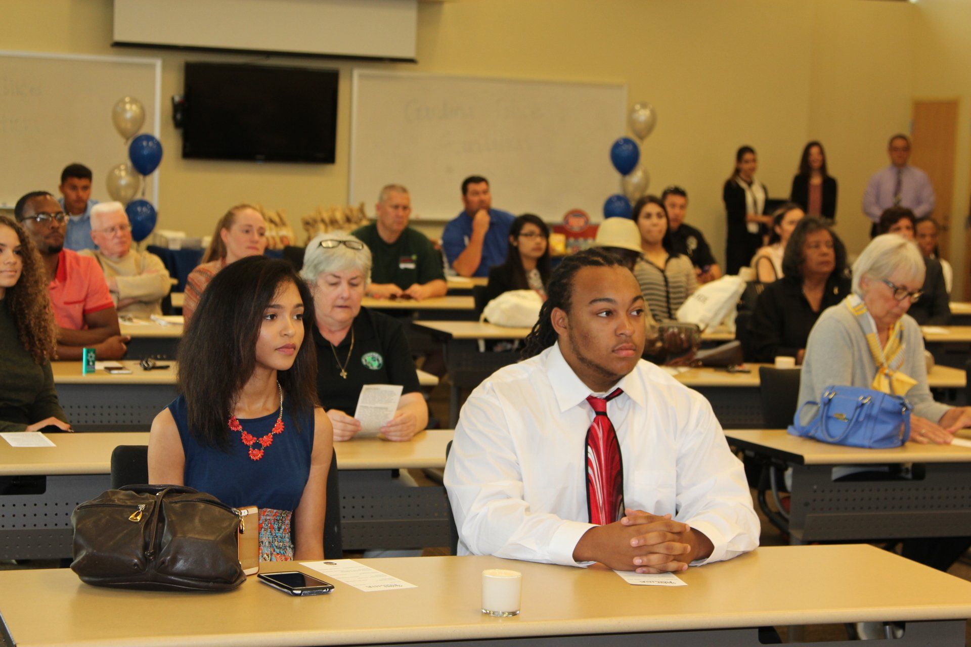 A group of people are sitting at tables in a classroom.