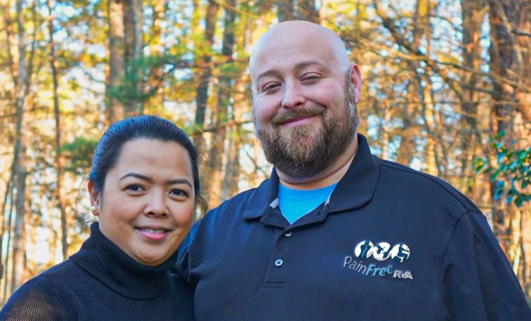 A man and a woman are posing for a picture in the woods.