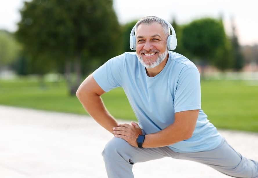 A man wearing headphones is stretching his legs in a park.