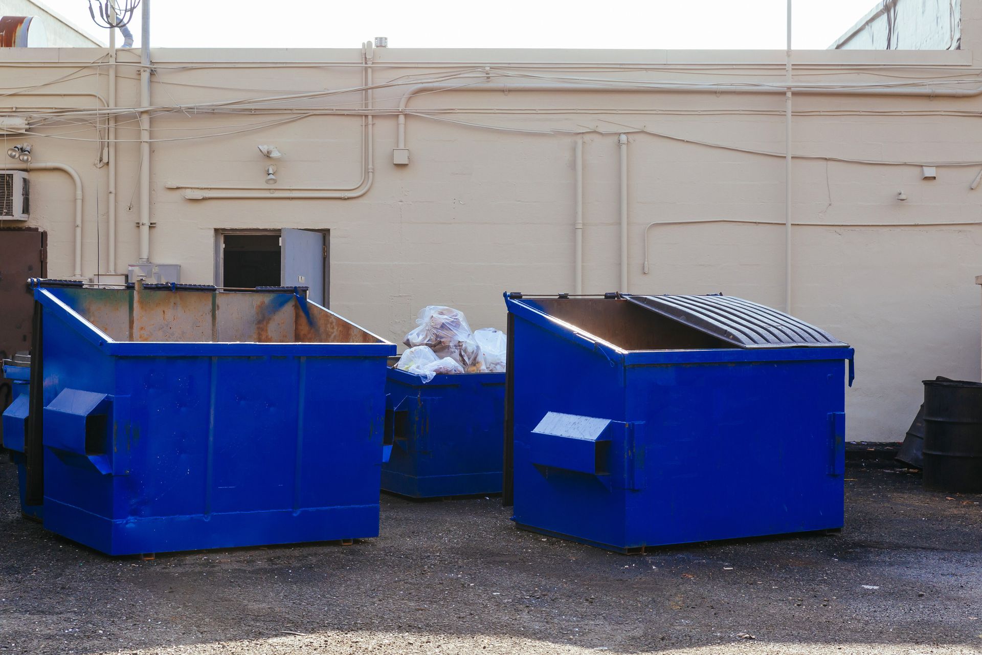 Two blue dumpsters are sitting in a parking lot in front of a building.