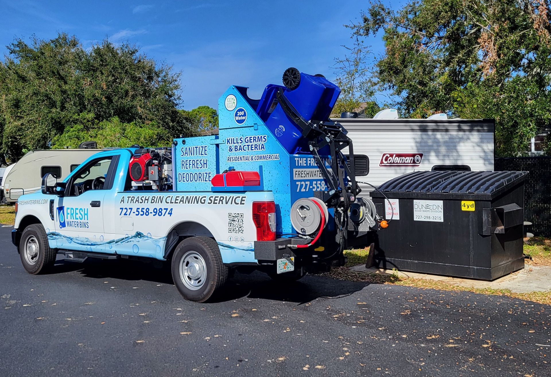 A couple of green trash cans filled with garbage next to a body of water.