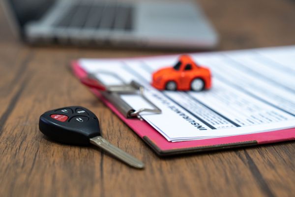 Una chiave di un'auto è appoggiata su un blocco per appunti accanto a una macchinina giocattolo.
