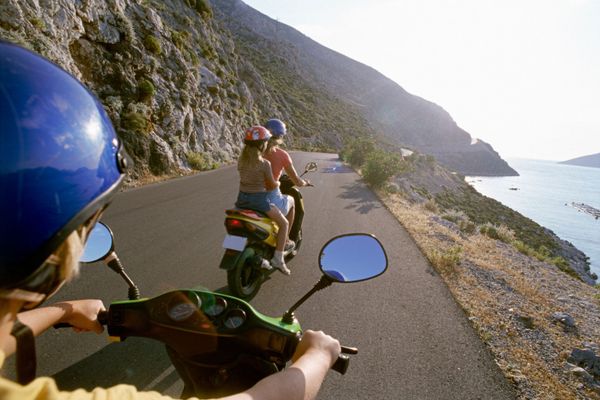 Un gruppo di persone sta guidando degli scooter lungo una strada vicino all'oceano