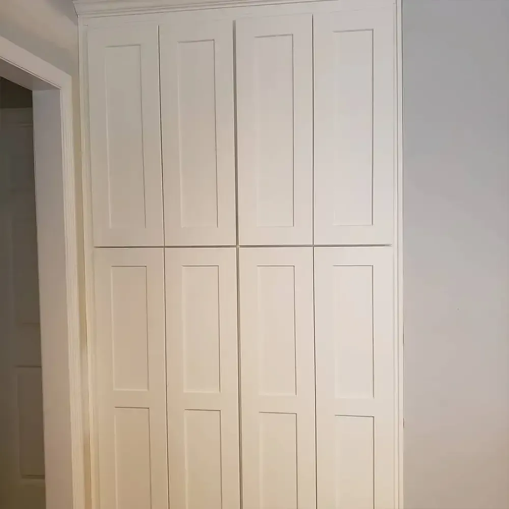 White built-in storage cabinet with eight doors against a light gray wall. The cabinet is next to a doorway.