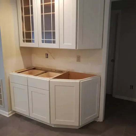 White kitchen cabinets being installed against a pale yellow wall. Lower cabinets have an angular corner.