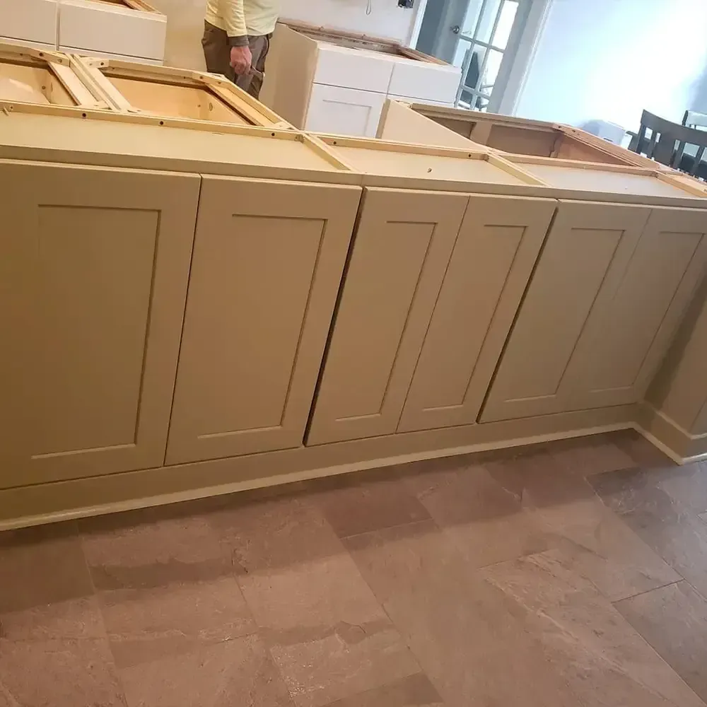 Cabinets are being installed on a floor with a person standing nearby. The cabinets are a light green color.