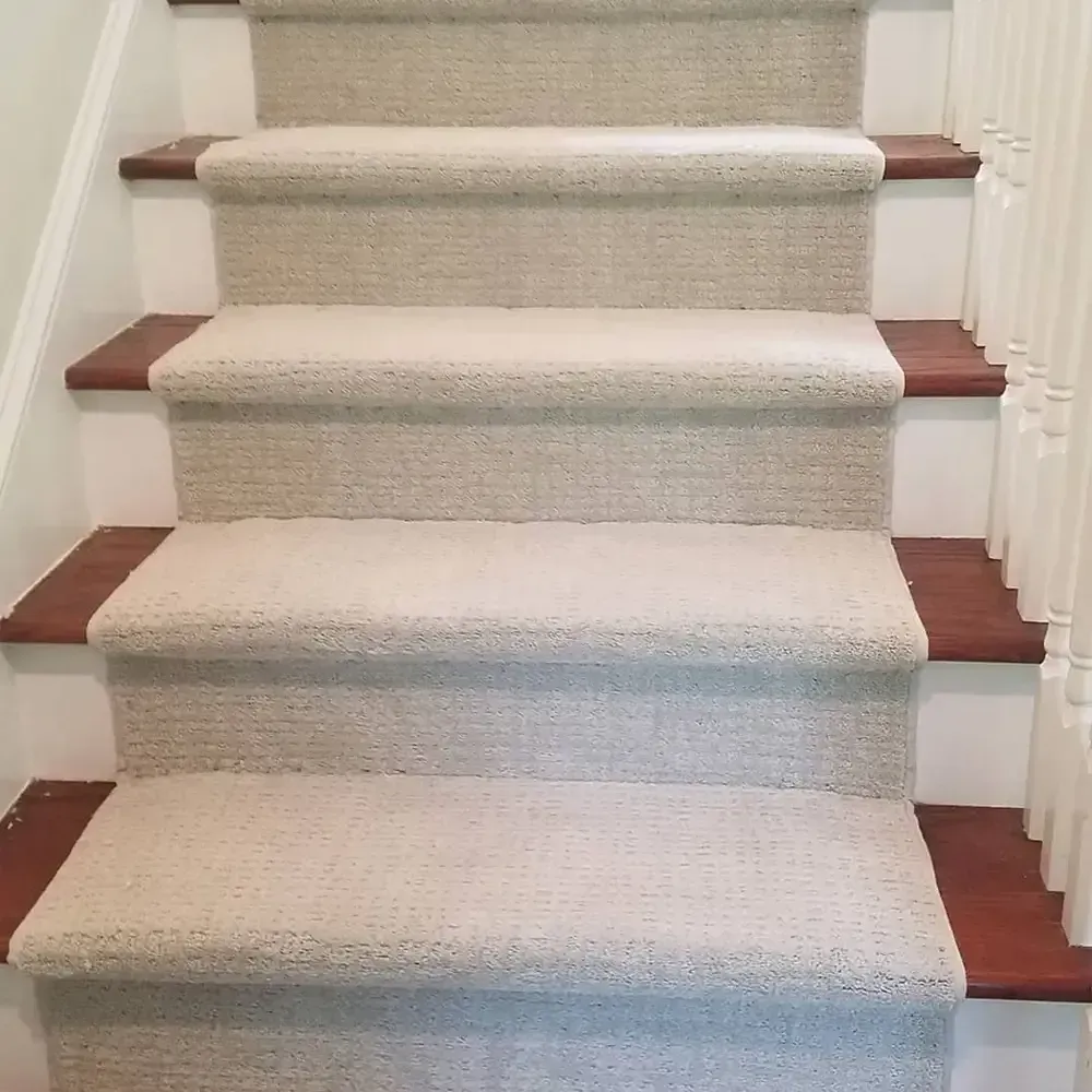Staircase with beige carpet runners on wooden steps. White risers and dark wood on the sides and treads.