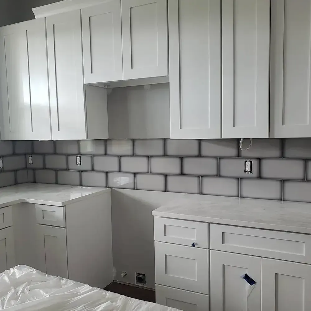 White kitchen cabinets and countertops with a gray brick-like backsplash.