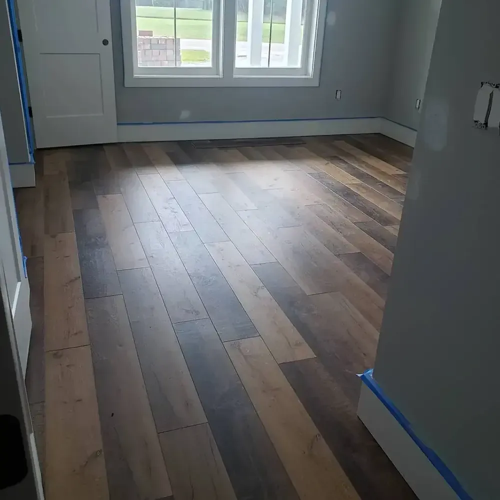 A room with newly installed wooden flooring. Gray walls and white trim surround the floor, and a window offers a view.