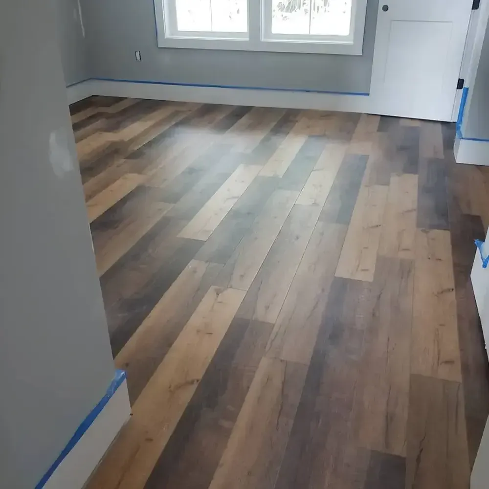 Newly installed hardwood-look laminate flooring in a room with gray walls, white trim, and a closed white door.