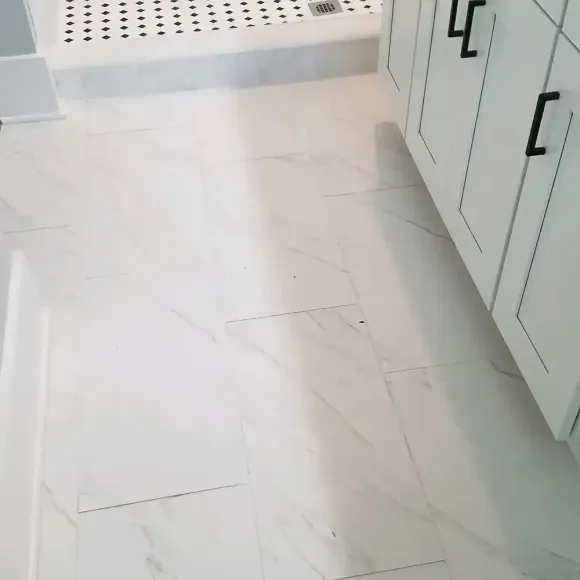 White marble bathroom floor with white cabinets and black hardware; shower in the background.