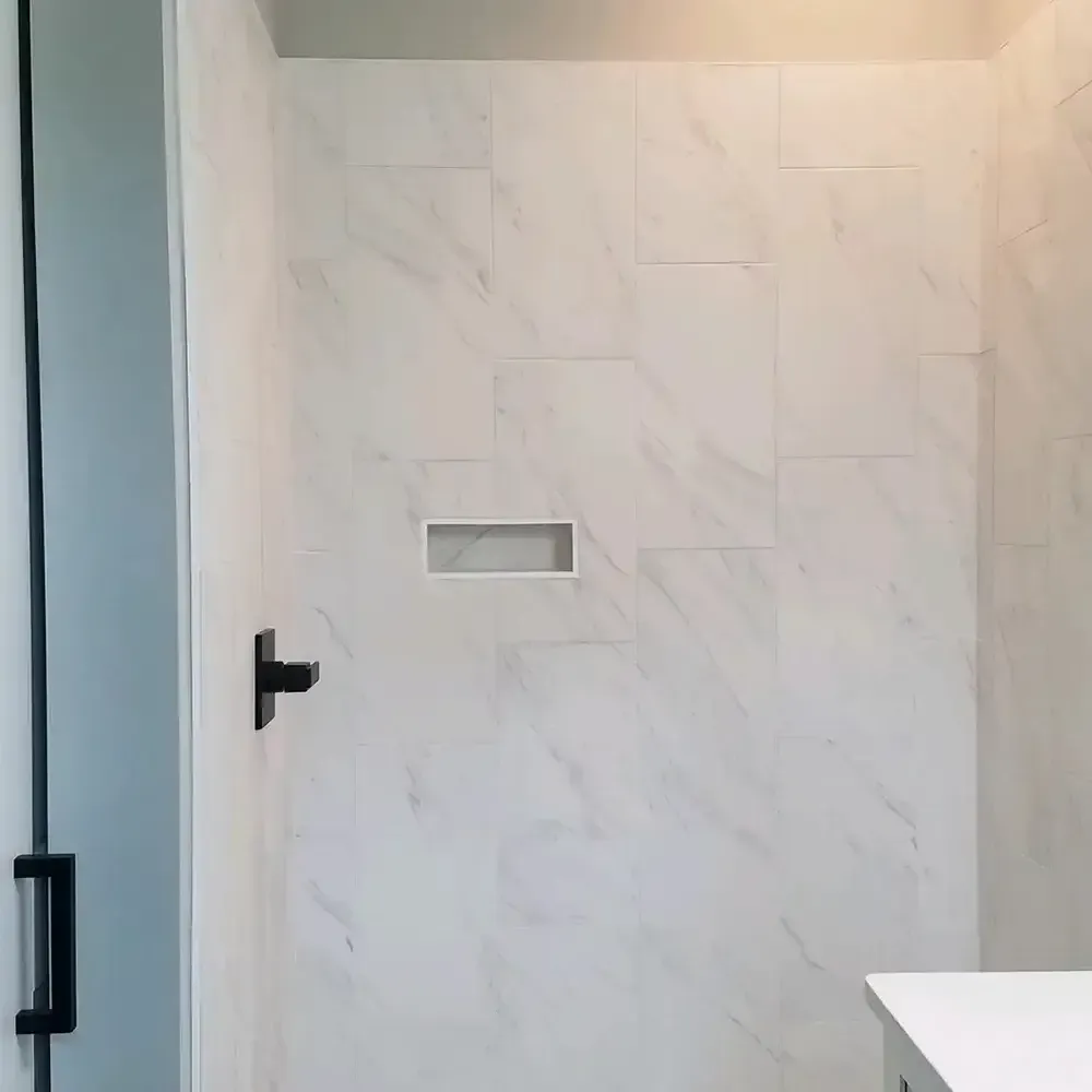White-tiled shower interior with a recessed shelf and black hardware, including a handle and shower controls.