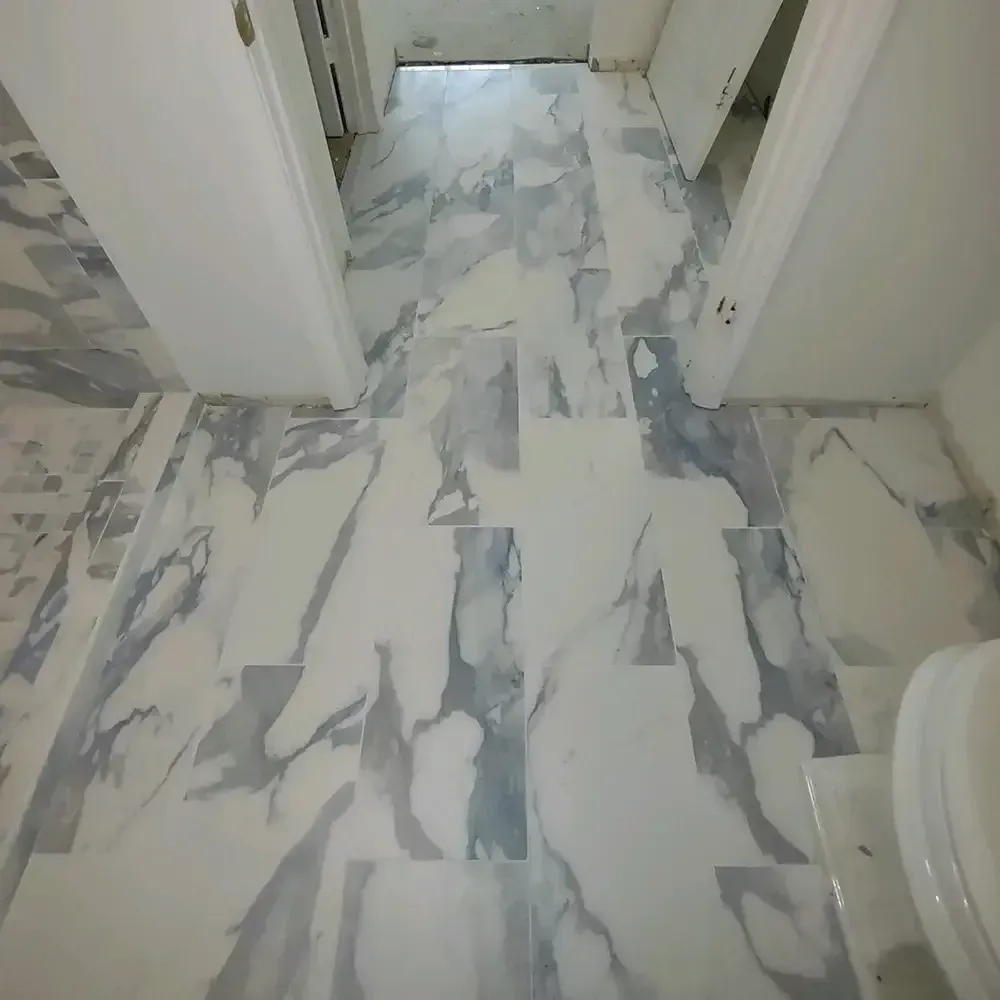 Bathroom floor with white marble tile and grey veining; showing a toilet on the right and doorways on either side.