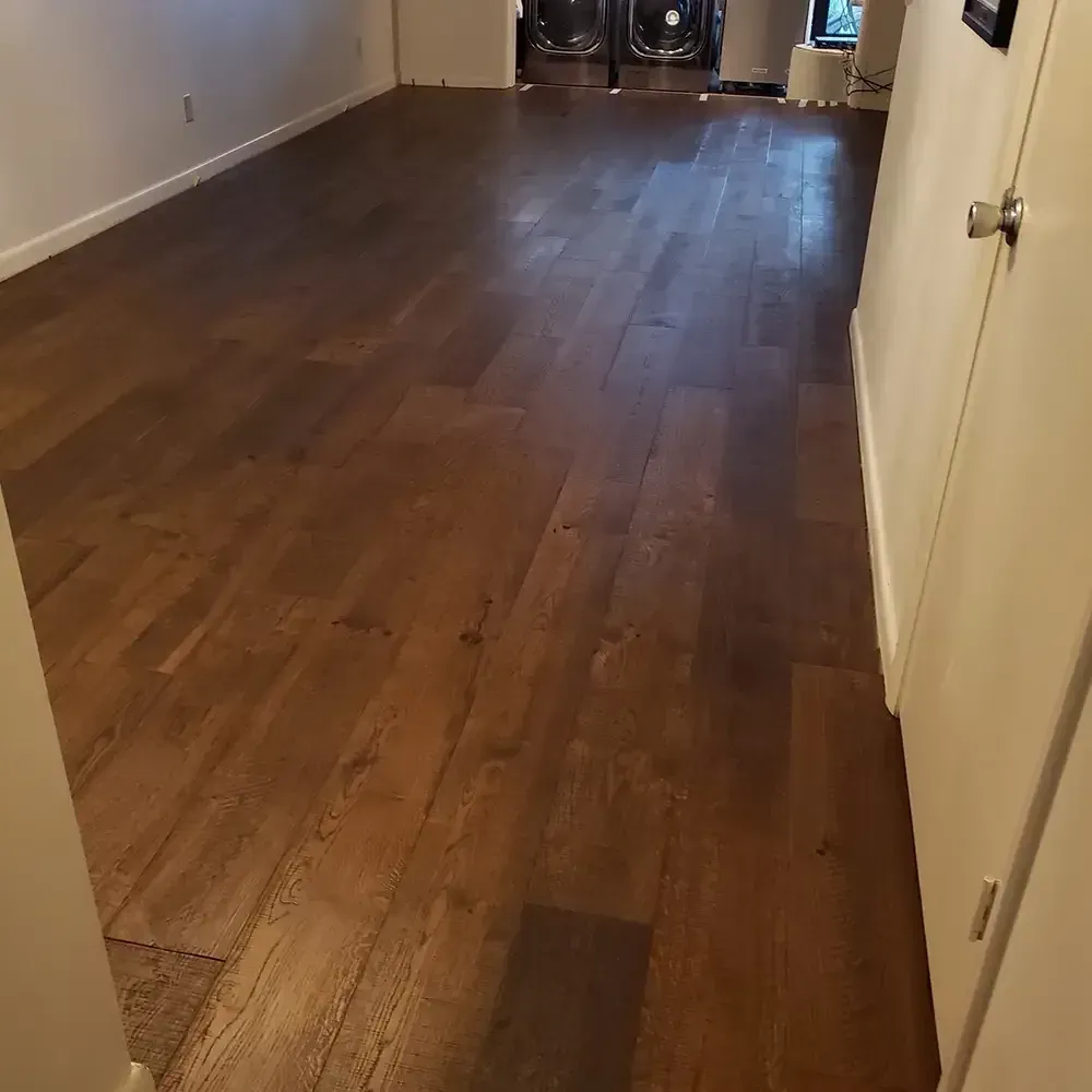 Wooden floor in a room with white walls, leading towards a darker area. A door is on the right.