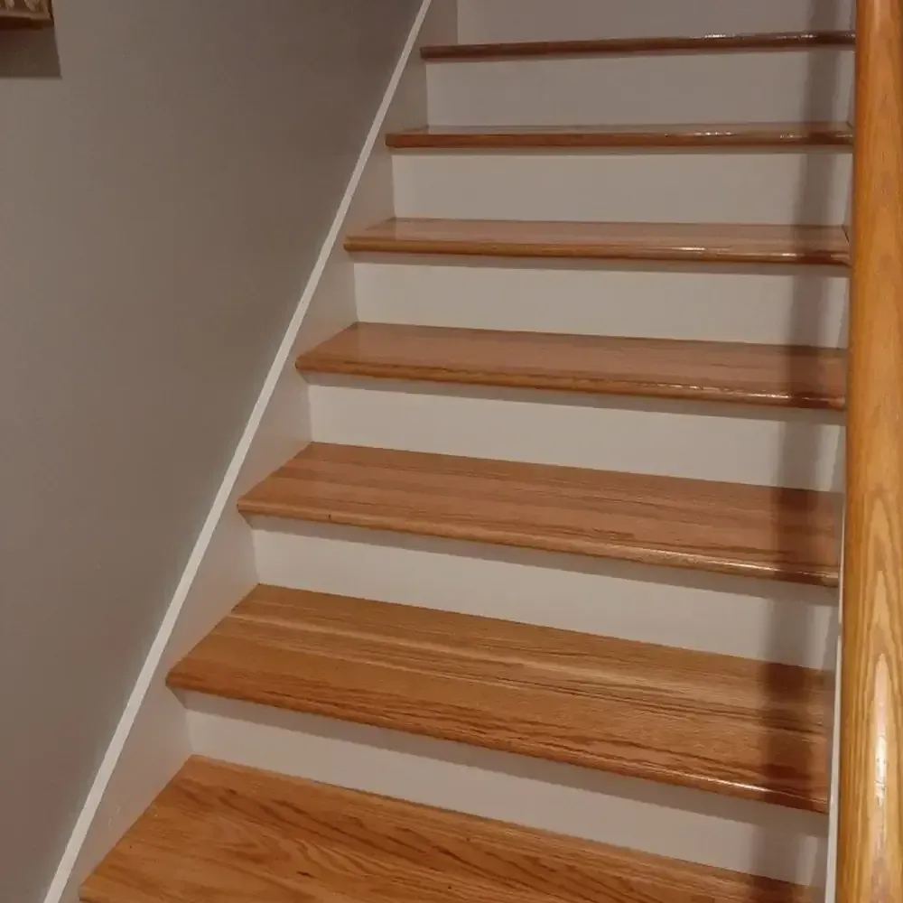 Wooden staircase with white risers and a wooden handrail against a gray wall.