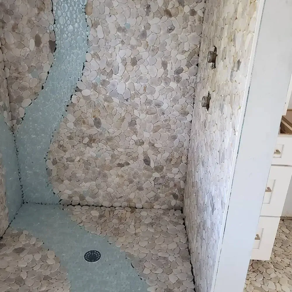 Shower with pebble tile walls and a light blue river design. The shower has a white frame and three holes.