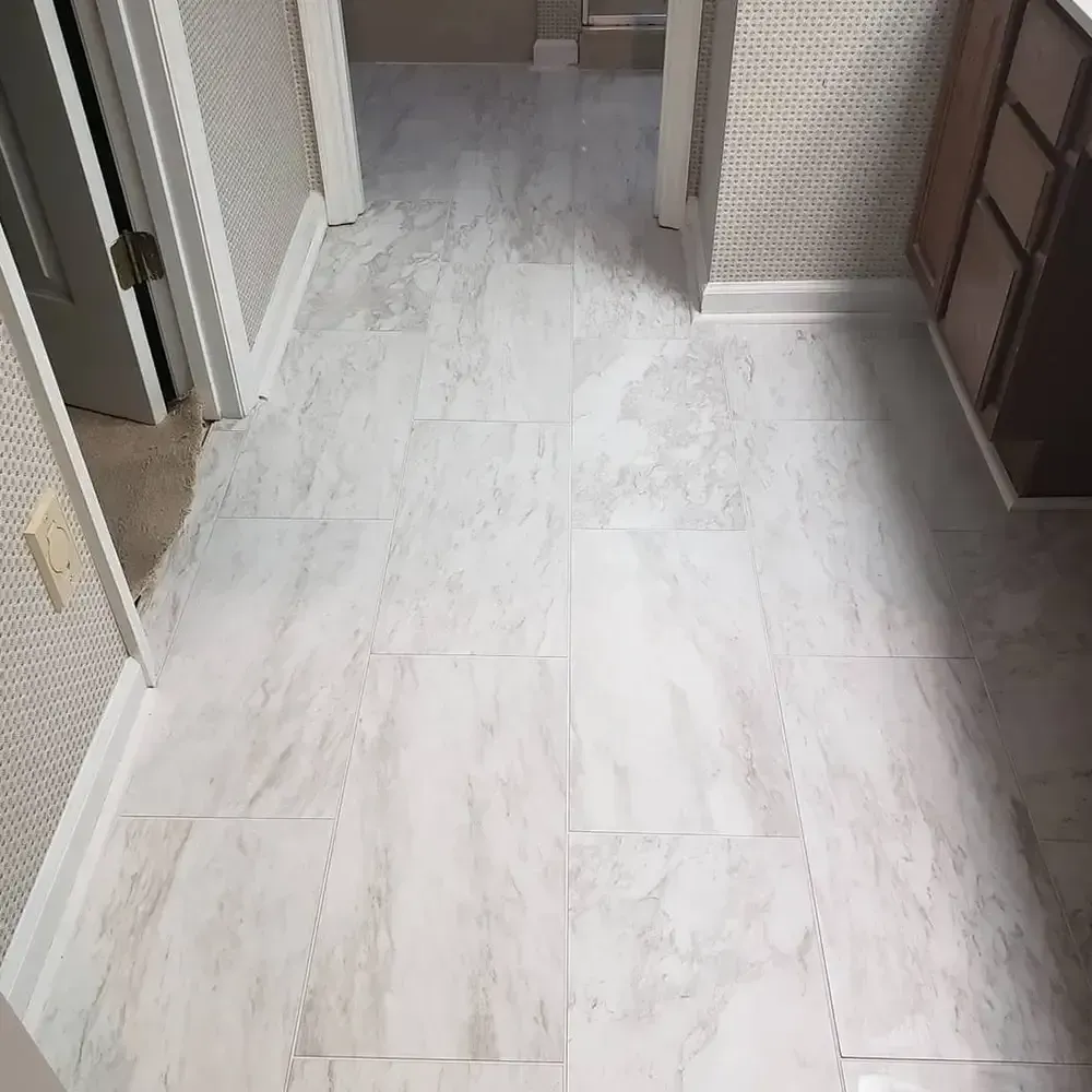 Hallway with light grey marble-look flooring. Walls are wallpapered in a textured white pattern, with a partially visible doorway and cabinet.