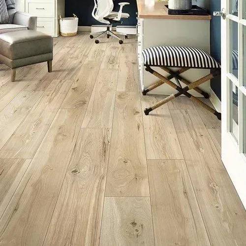 Light-colored wooden floor in a well-lit room with furniture, including a desk, chair, and ottoman. A doorway is visible on the right.