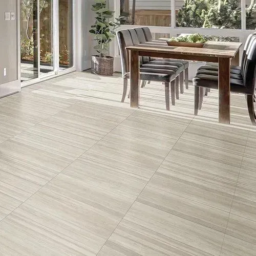 A light-colored dining room with a wooden table, chairs, and tile flooring; sunlight streams in from a glass door.