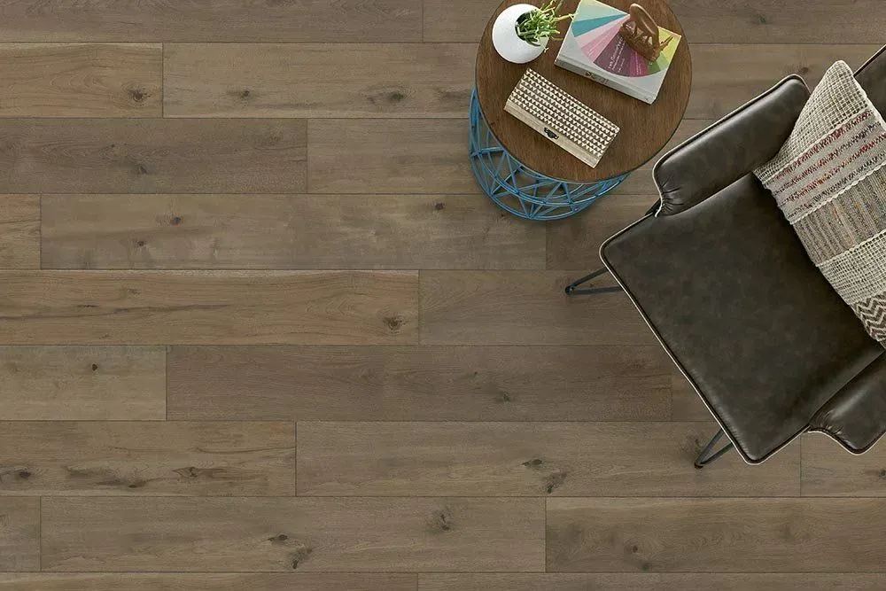 Wooden floor with a chair and side table. The table has a book, plant, and clutch.