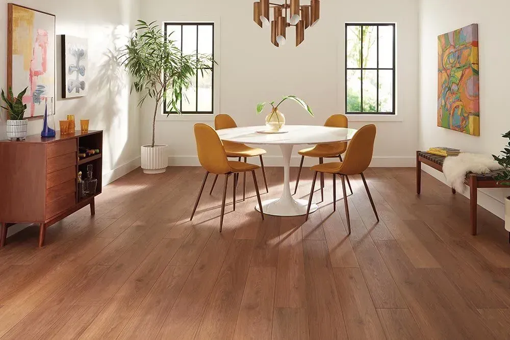 Dining room with hardwood floors, a white table, yellow chairs, and decorative art and furniture. Natural light floods the room.