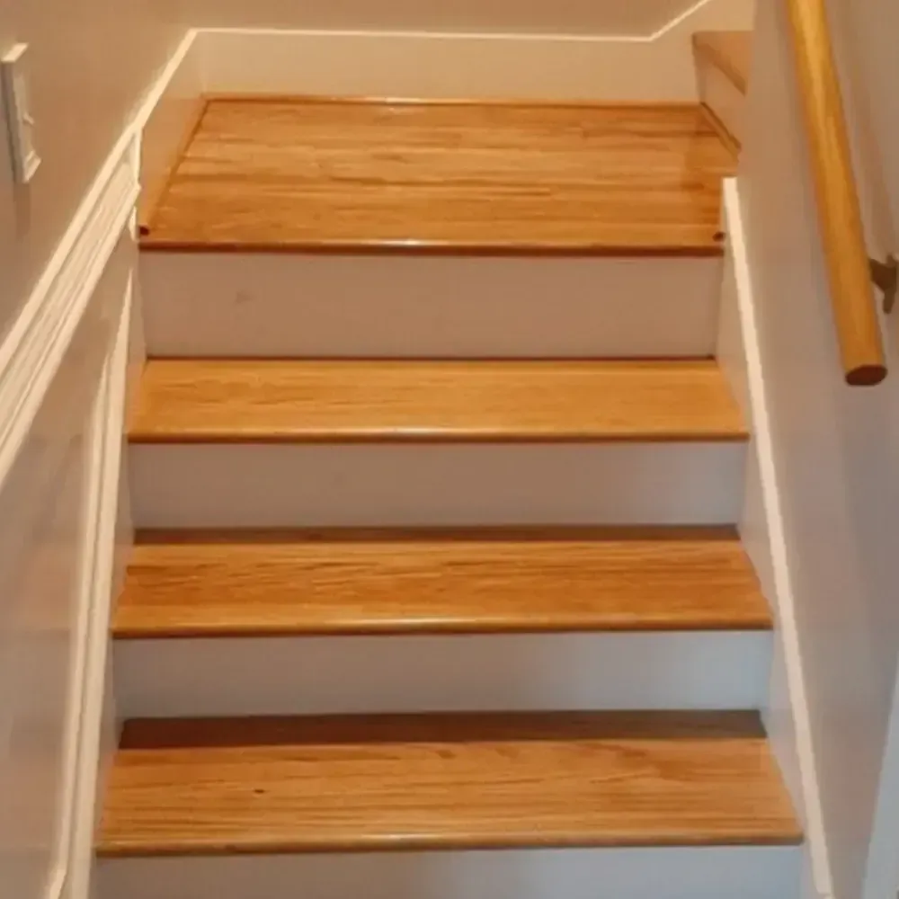 Wooden staircase with white risers, a wooden handrail on the right, and white walls.