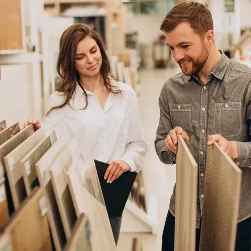 A couple looking at tile samples in a store; woman in white shirt and holding clipboard, man in gray shirt.