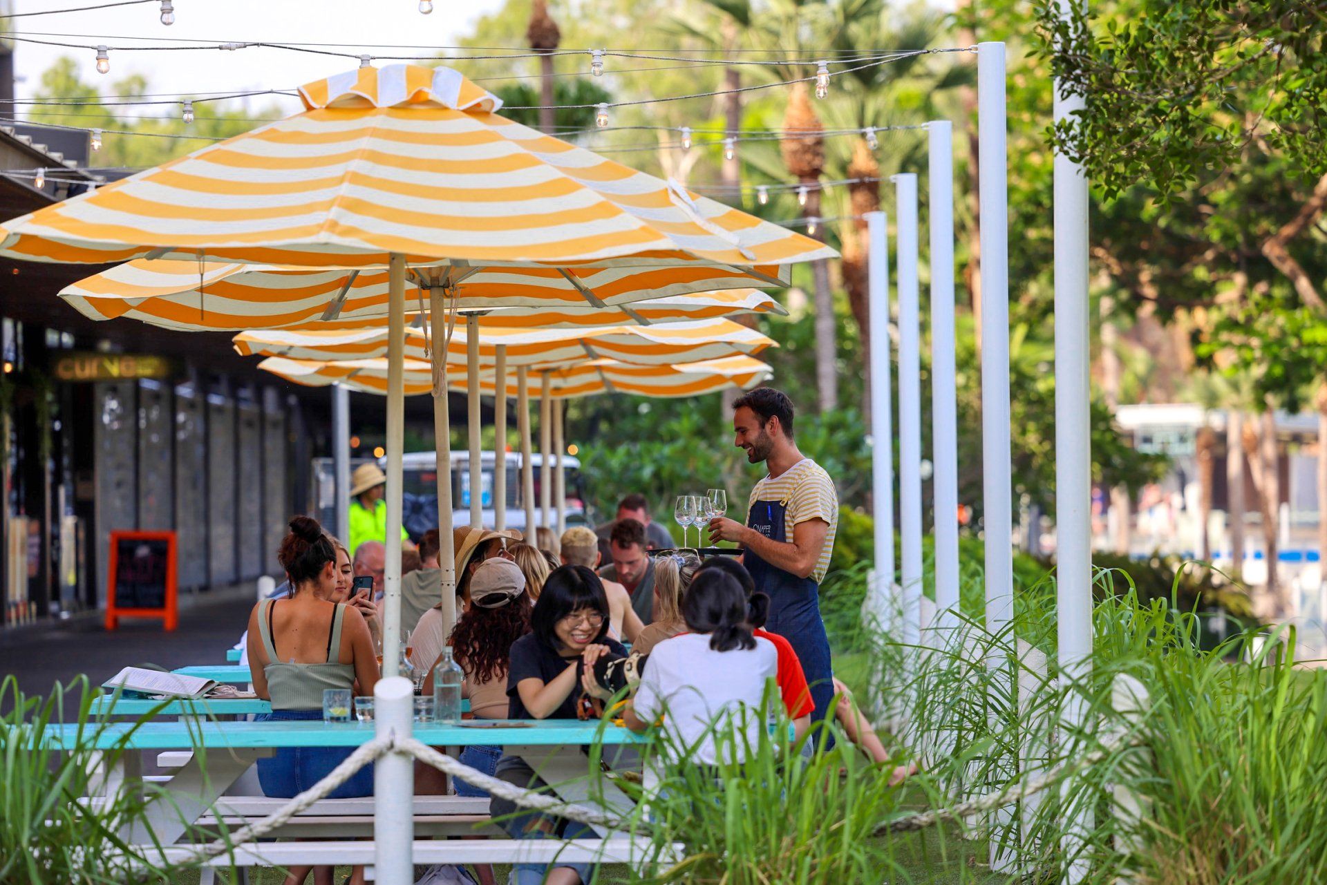 A waiter takes a tables order at Snapper Rocks with yellow and white striped umbrellas overhead