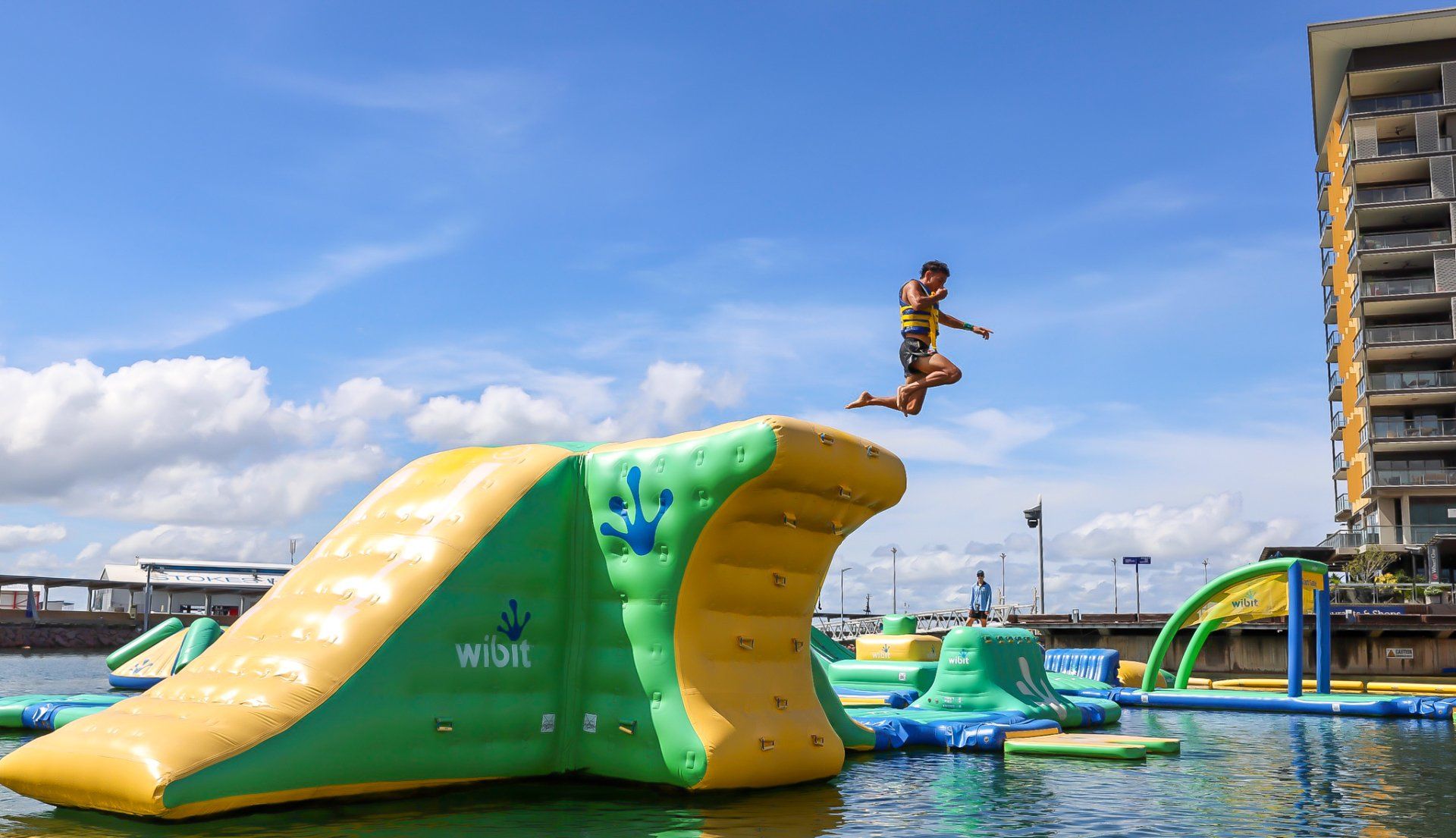 A young man jumps off of the Wibit Aqua Park into the water