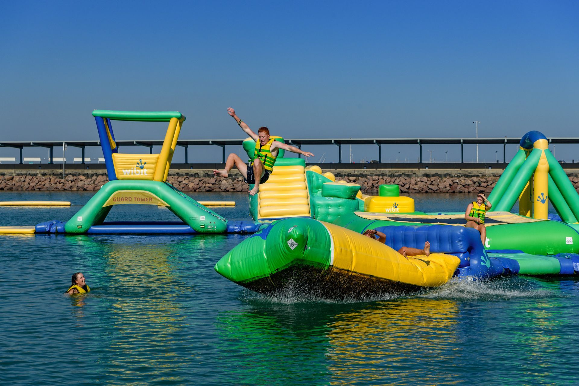An image of the inflatable Aqua Park with a young man bouncing off the large jumping pillow. The words ' Aqua Park' are written over the image.